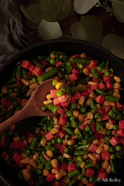 a wooden spoon scooping some veggie medley from a frying pan