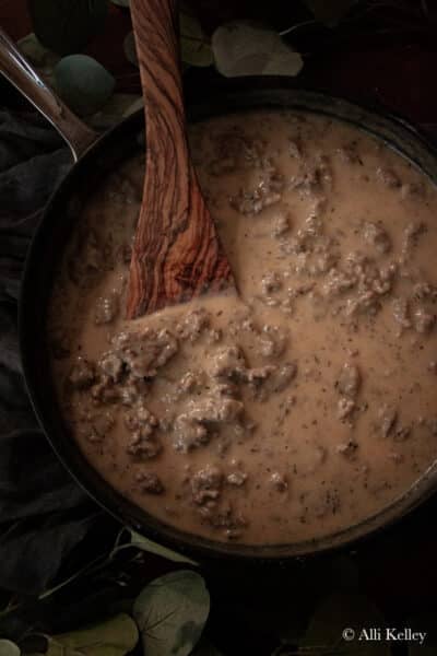 a wooden spatula mixing homemade sausage gravy in a frying pan