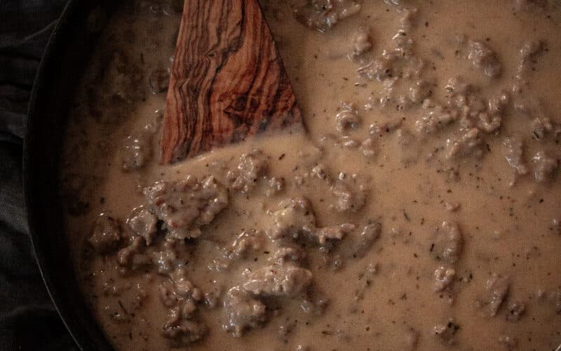 a wooden spatula mixing homemade sausage gravy in a frying pan