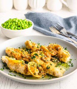 a plate of easy chicken piccata with peas in the background.