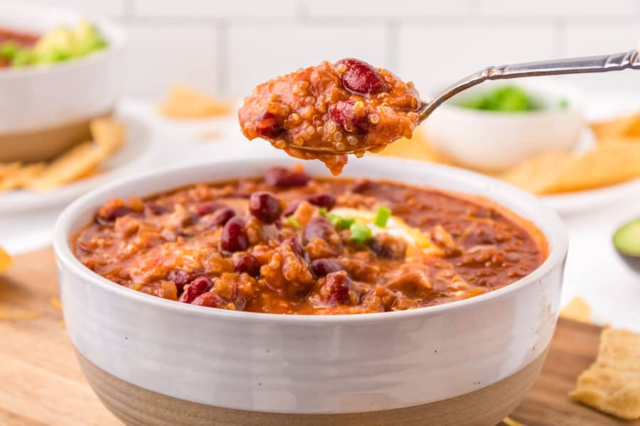 A bowl of chili topped with beans and green onions, with a spoonful of this good vegetarian chili recipe held above the bowl. Tortilla chips and a bowl of green onions are visible in the background.
