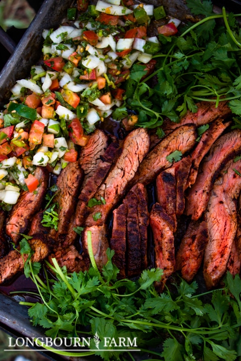Sliced grilled steak seasoned with Tex Mex seasoning, served with fresh tomato salsa and garnished with cilantro, displayed on a tray. The Longbourn Farm logo is visible at the bottom.