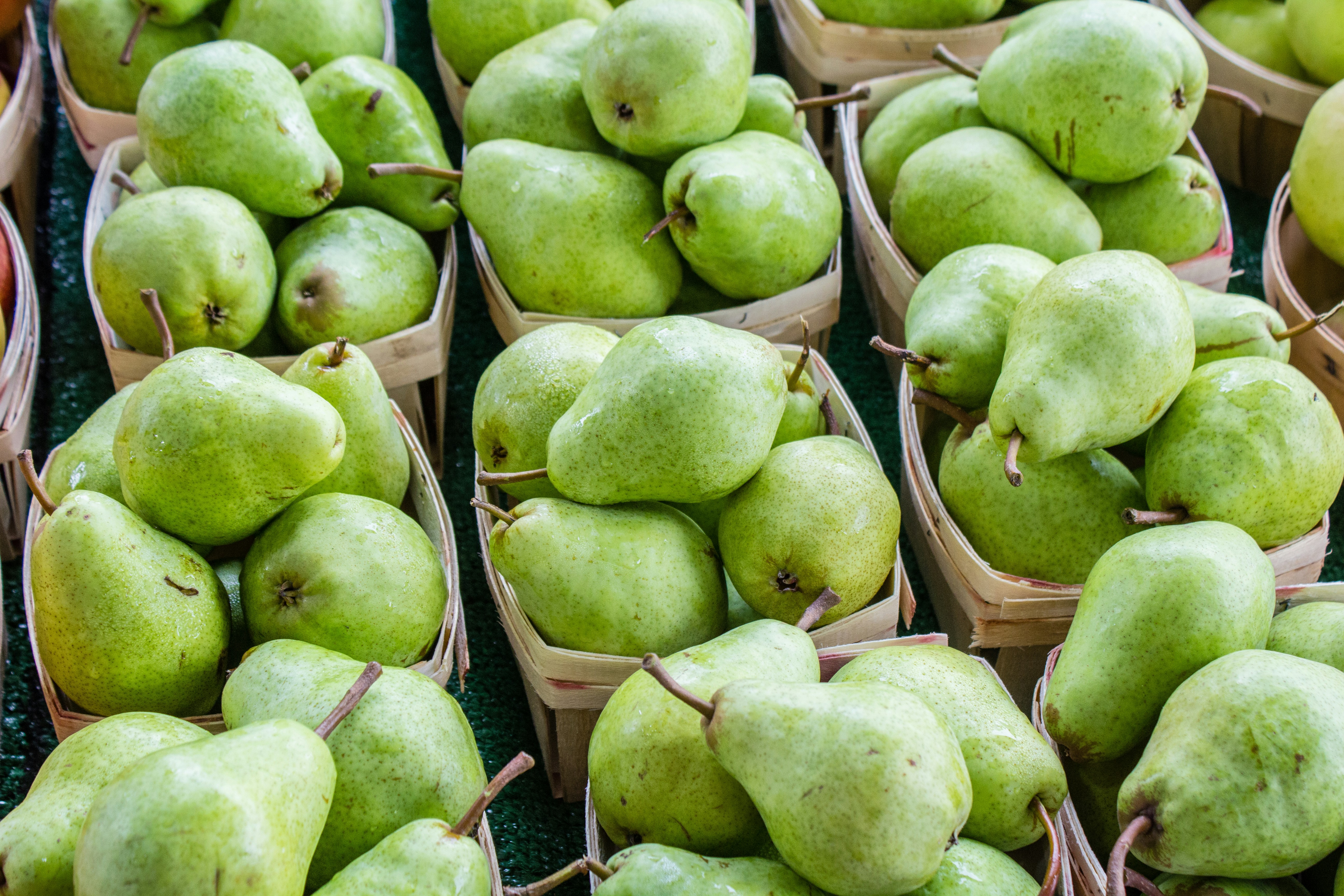 Multiple small wooden baskets filled with fresh green pears are arranged in rows on a market stand.